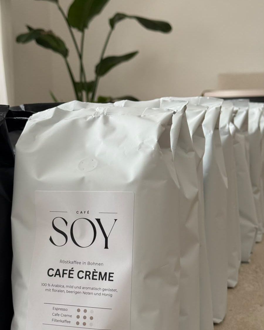 Eine Reihe weißer Café-Crème-Tüten von Café SOY vor einer grünen Pflanze